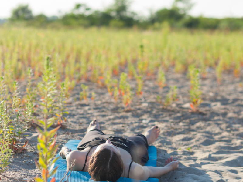 Woman laying on a yoga mat preparing for yoga Nidra in the sand,
