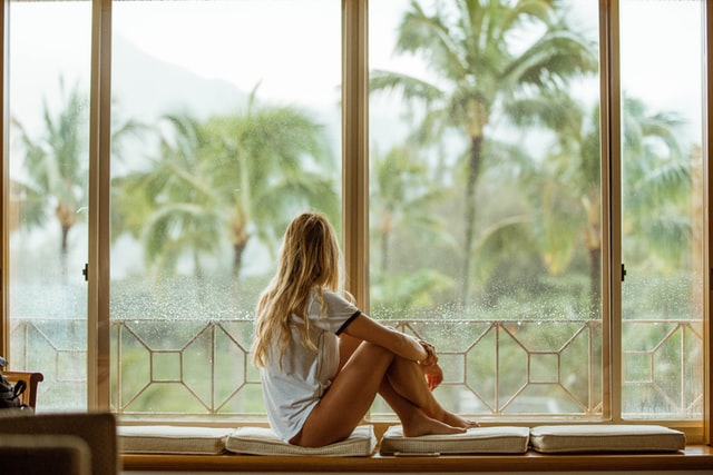Girl looking out of a large window with palm trees