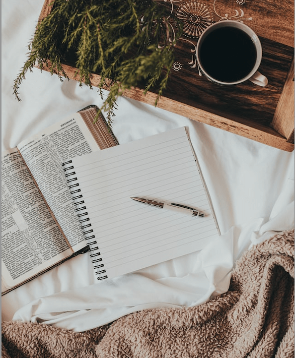 Journal by a cozy blanket and cup of coffee on a wooden tray with ferns